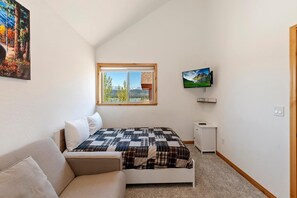 A bedroom with a bed, a window with a view, a television, and a small bedside table.
