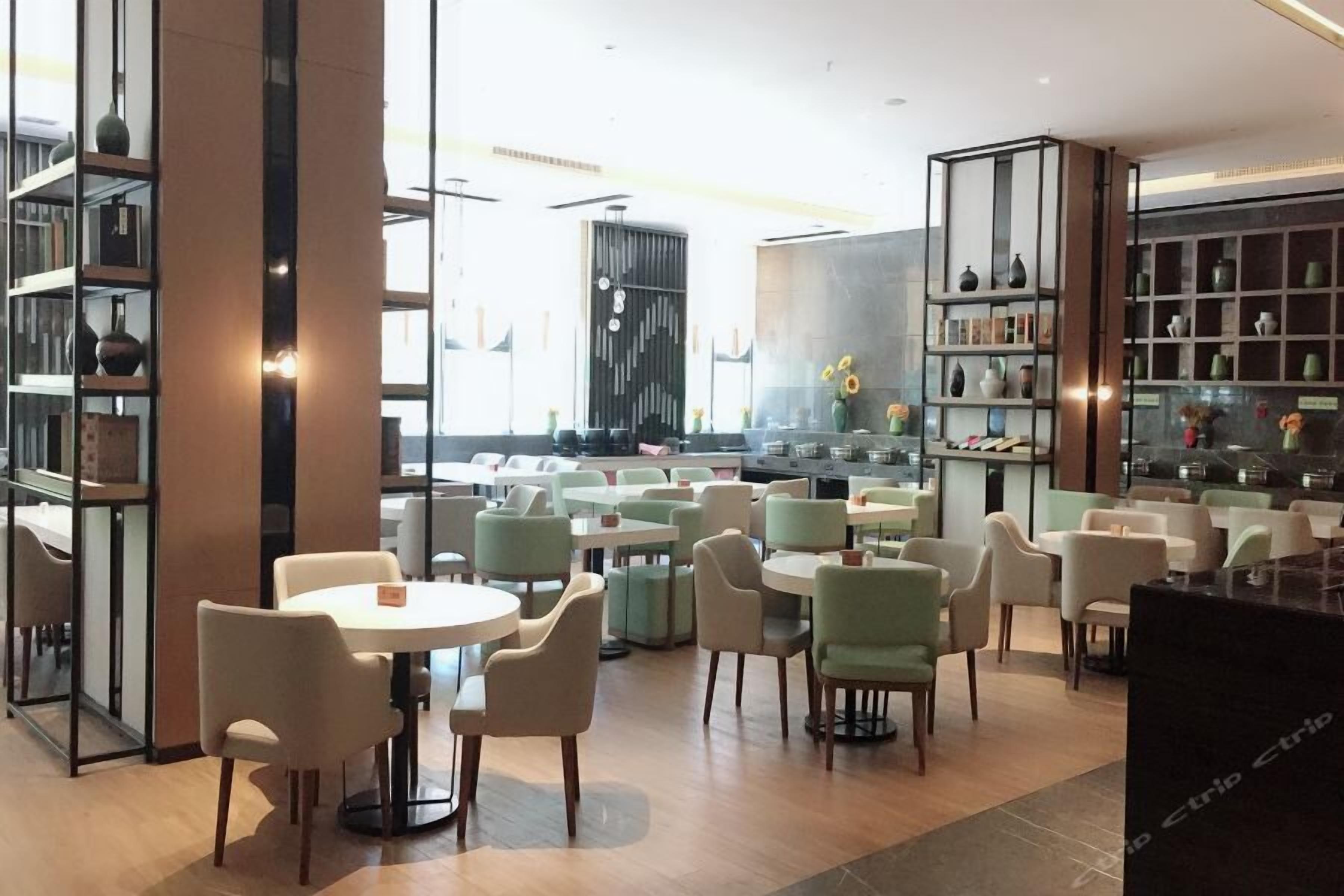 Un café moderno con mesas y sillas redondas, una zona de cocina y estantes con objetos decorativos.