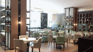 Un café moderno con mesas y sillas redondas, una zona de cocina y estantes con objetos decorativos.