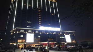 Un hotel de varios pisos con señalización iluminada y un área de estacionamiento al frente.