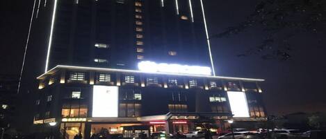 A multi-story hotel with illuminated signage and a parking area in front.