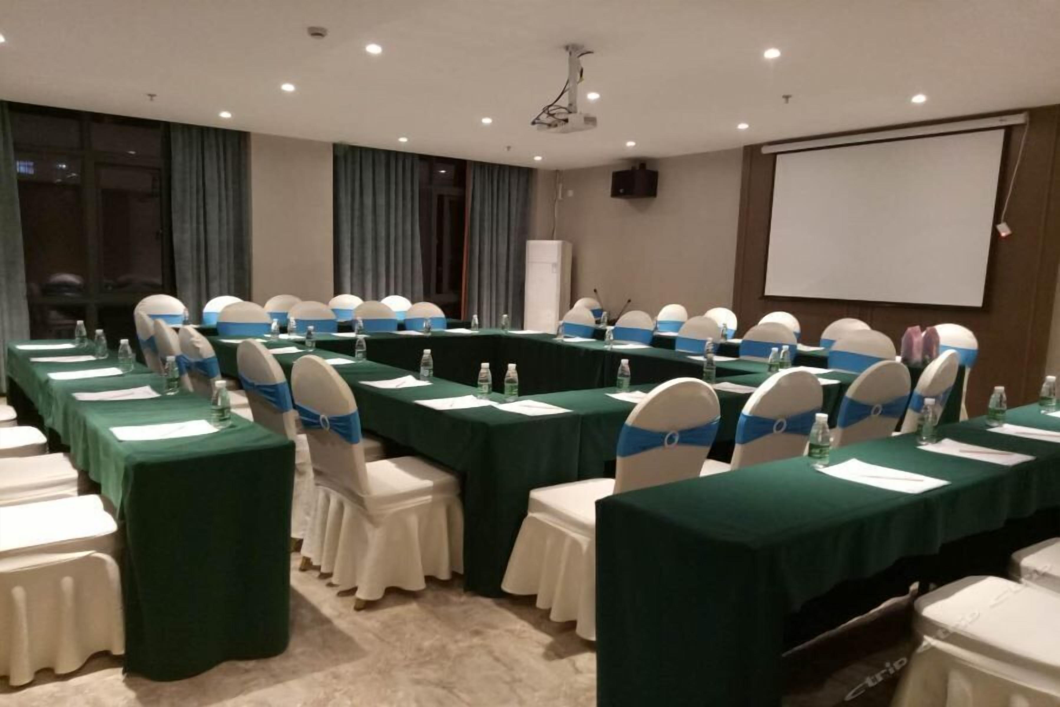 Un salón de conferencias con largas mesas, sillas y una pantalla para proyector.
