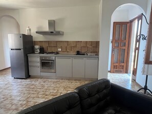 Une cuisine moderne équipée d’un réfrigérateur, d’un four et d’une cuisinière, un coin repas avec un canapé et une vue sur une porte en bois.