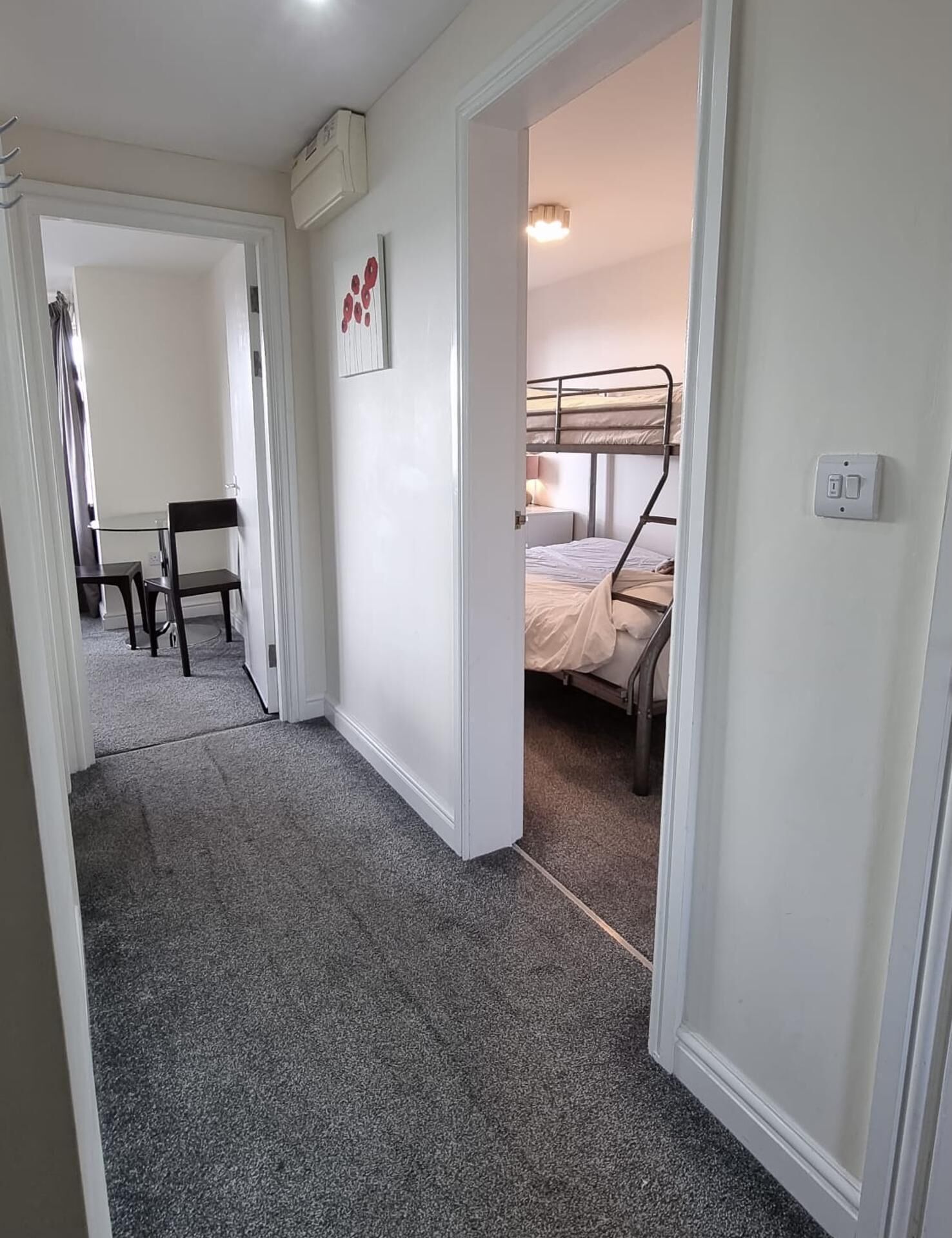 A hallway leading to a bedroom with a bunk bed, a desk with a chair, and a framed picture on the wall.
