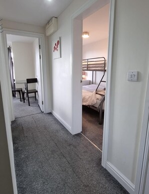 A hallway leading to a bedroom with a bunk bed, a desk with a chair, and a framed picture on the wall. - Beachside Home - Sleeps 5, Garden, Parking & Pets (Skegness)