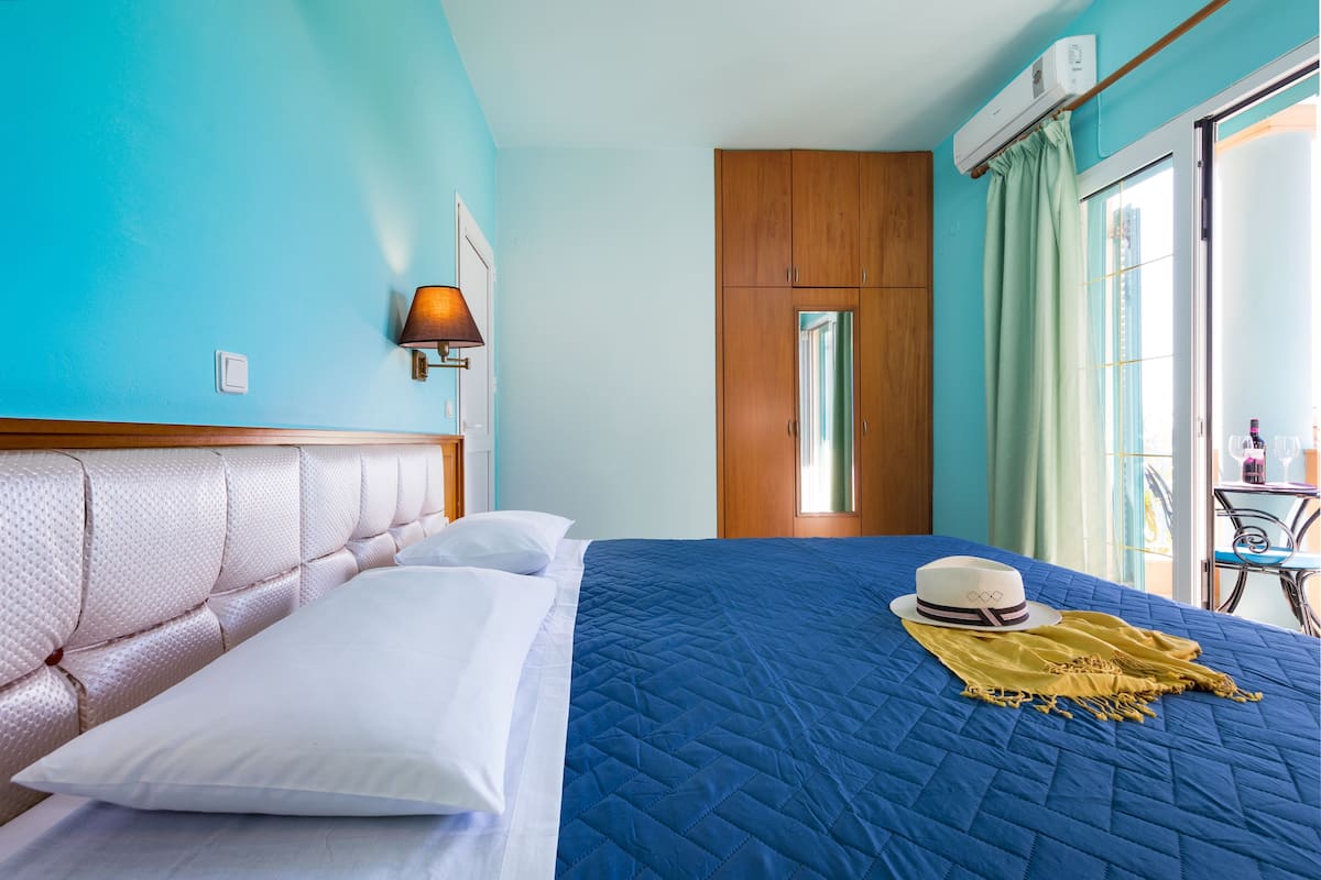 Ein Hotelzimmer mit blauer Bettdecke, einem weißen Kopfkissen, einem Holzkopfbrett, einer Wandleuchte und einem Fenster mit Vorhängen.