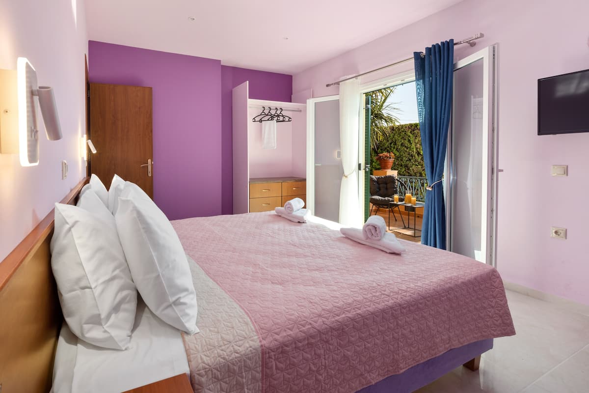 Ein Schlafzimmer mit Bett, einem Holzschrank, einem Badezimmer mit Spiegel sowie einem Balkon mit Tisch und Stühlen.