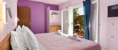 Ein Schlafzimmer mit Bett, einem Holzschrank, einem Badezimmer mit Spiegel sowie einem Balkon mit Tisch und Stühlen.