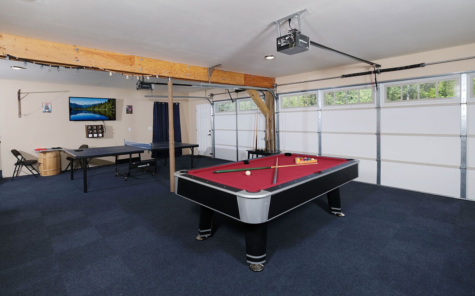 Una mesa de billar con superficie de fieltro rojo, una mesa de ping pong y un proyector montado en el techo.
