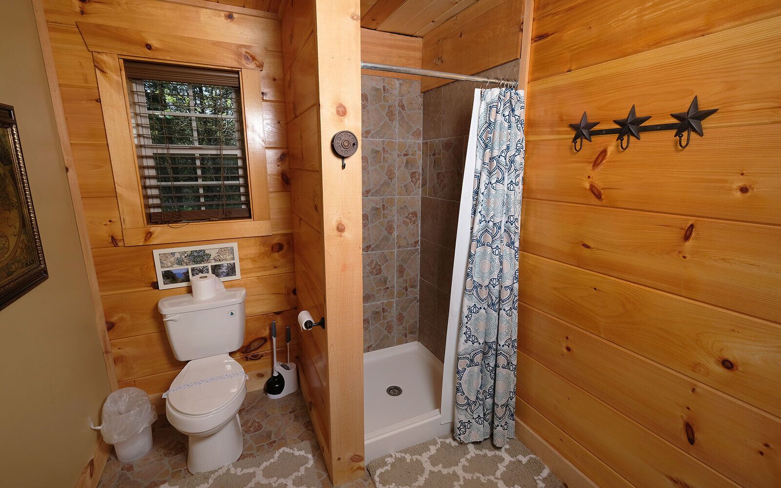 A wooden cabin bathroom with a toilet, shower, and a window.