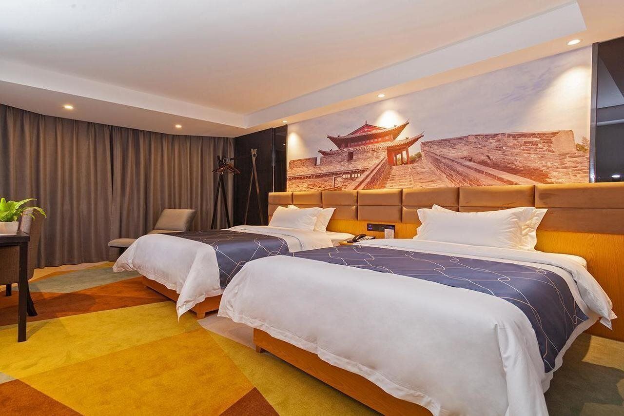 A hotel room with two beds, a large mural of a traditional building, a desk with a plant, and a chair.