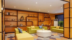 Un área de descanso moderna con sofás verdes, una mesa redonda de centro y estanterías de madera con objetos decorativos.