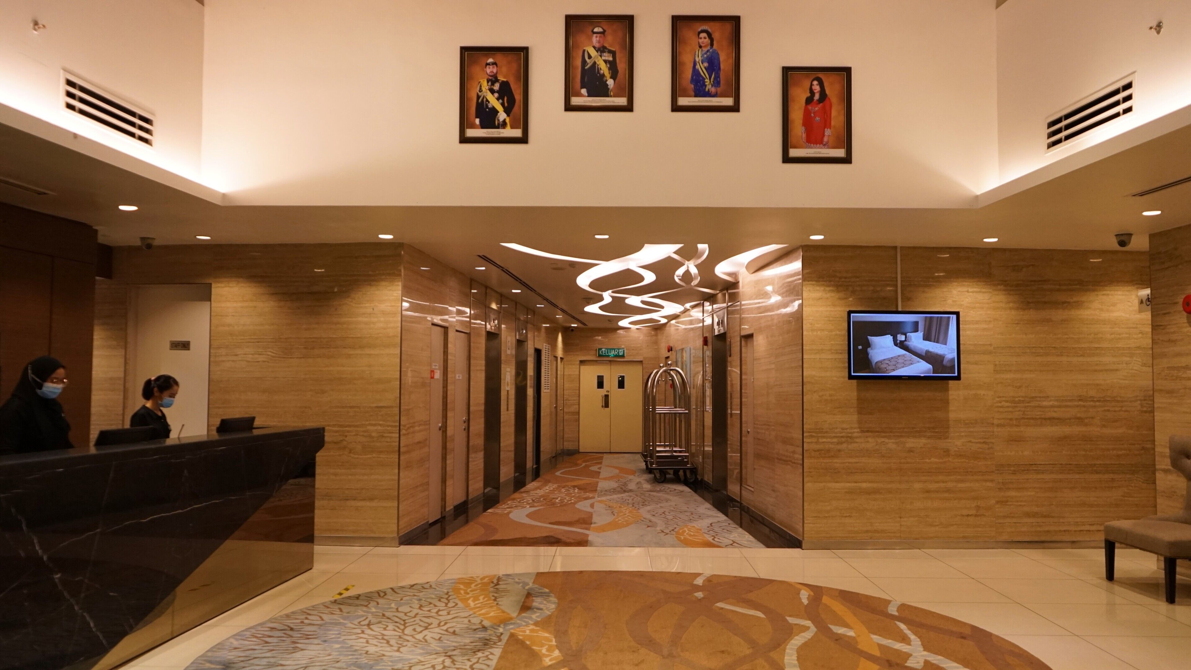 A hotel lobby with a reception desk, elevators, and a television screen.