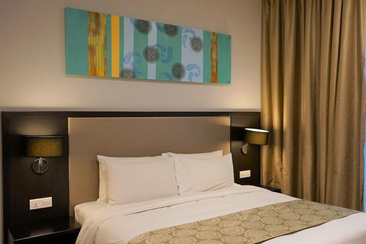 Habitación de hotel con una cama grande, dos lámparas de noche, una obra de arte en la pared y una ventana con cortinas.