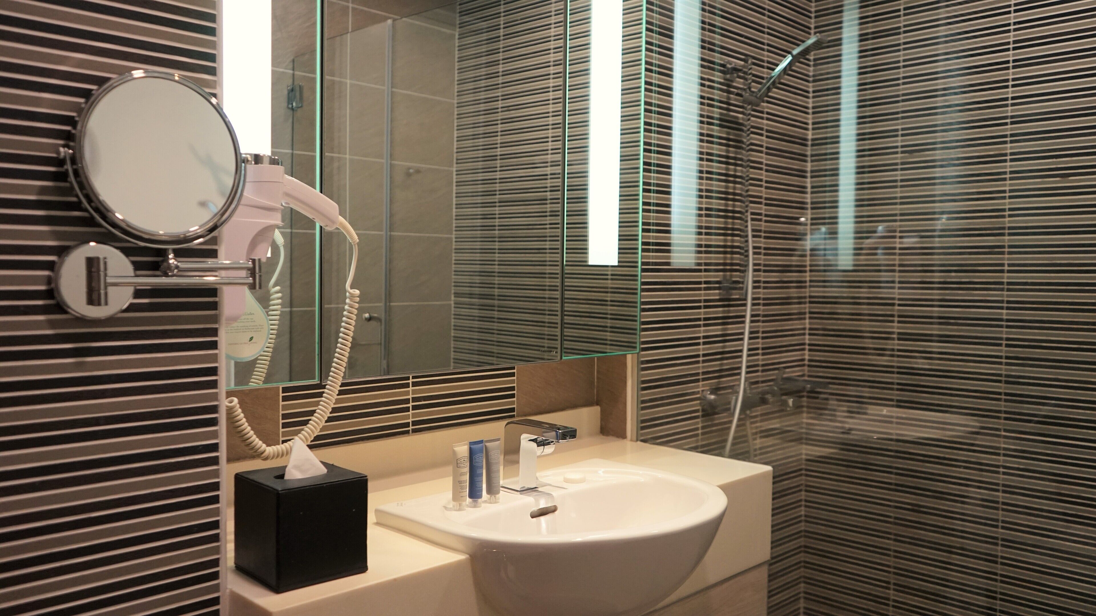 A modern bathroom with a large mirror, a hairdryer, a sink, and a shower.