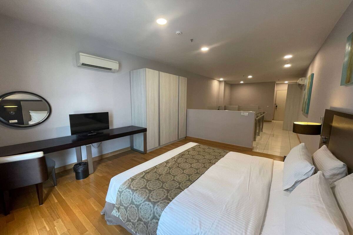 Habitación de hotel moderna con cama, escritorio, televisor y baño visible a través de una puerta abierta.
