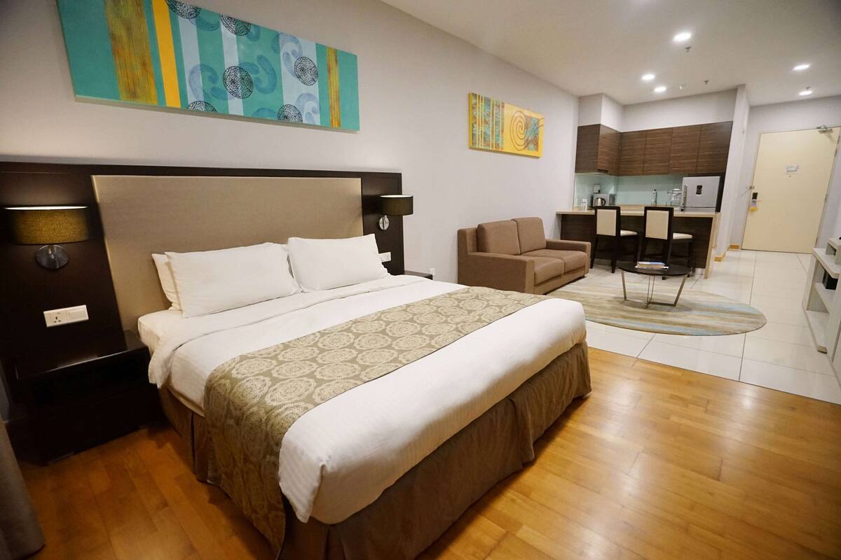 Habitación de hotel con una cama grande, un sofá, una mesa de comedor y una zona de cocina.