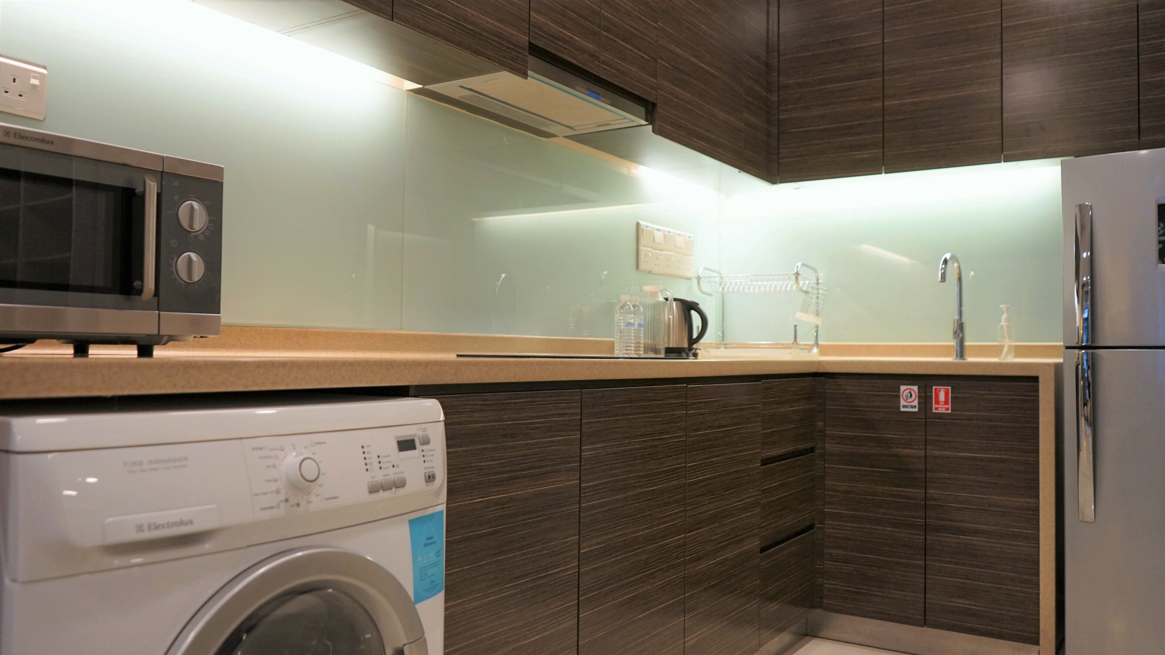 A modern kitchen with a washing machine, microwave, and refrigerator.