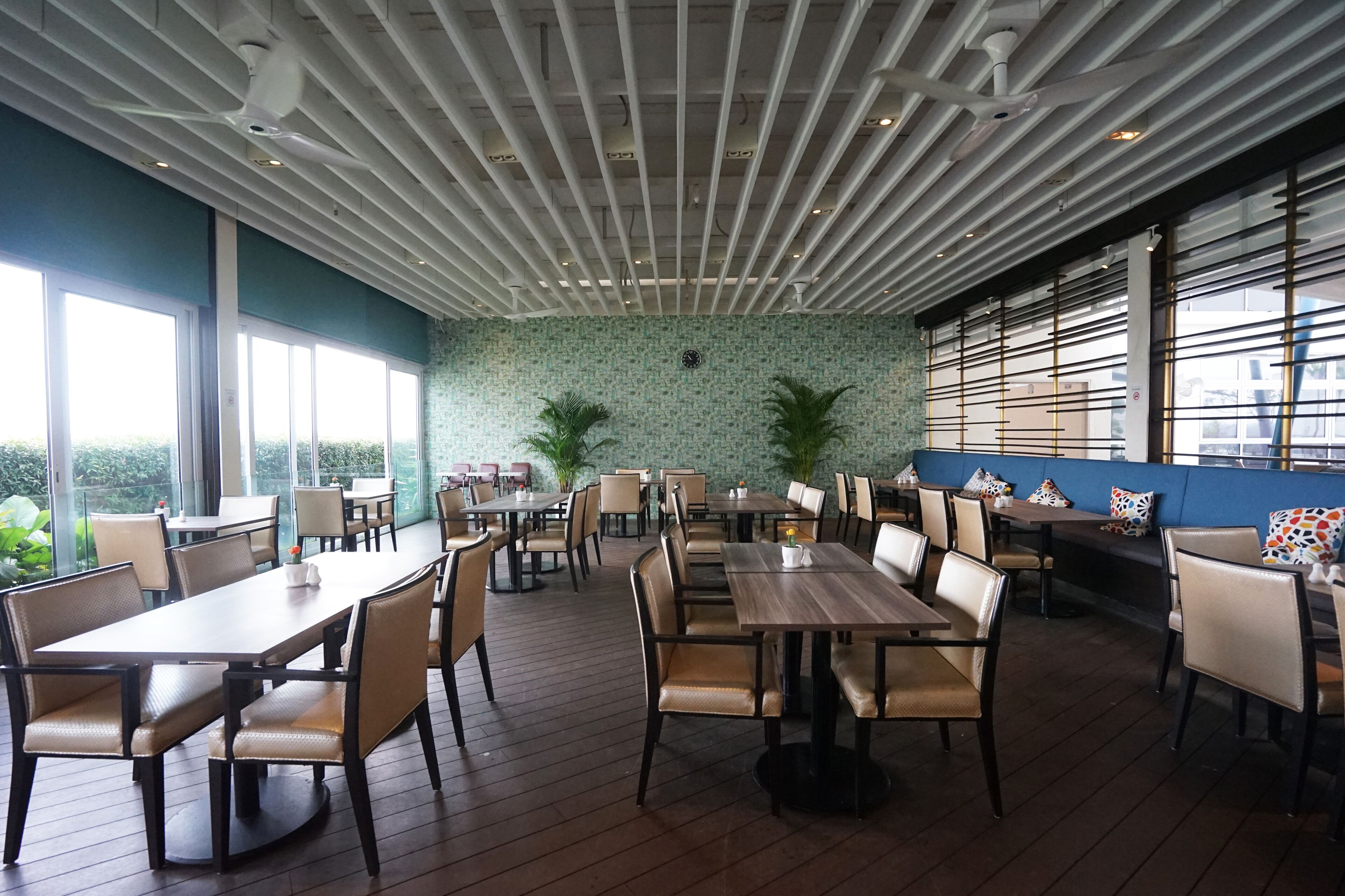 A restaurant with multiple tables and chairs, a ceiling with exposed beams, and large windows providing natural light.