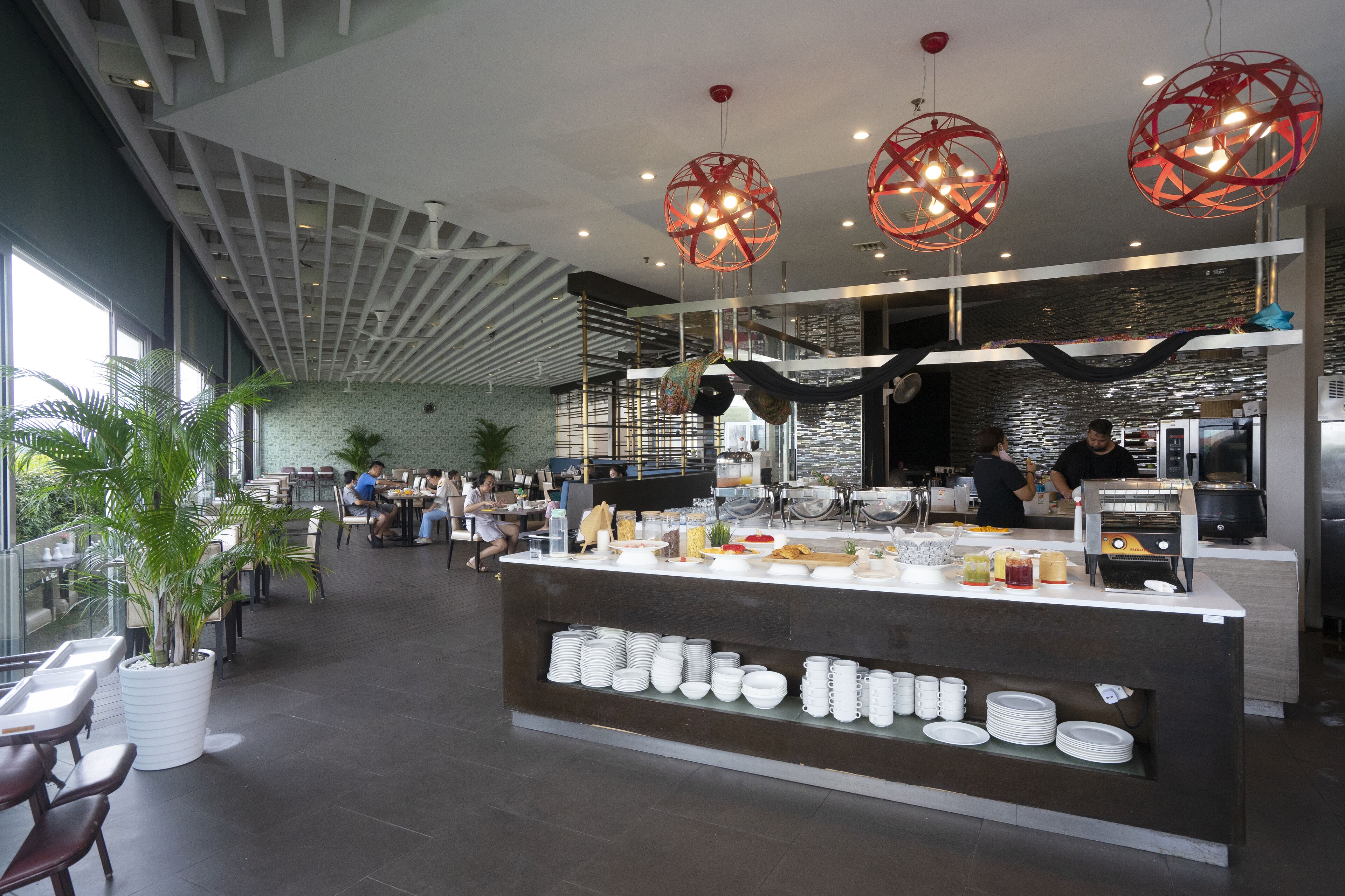 A modern cafe with a central counter displaying food and beverages, surrounded by seating areas with tables and chairs.