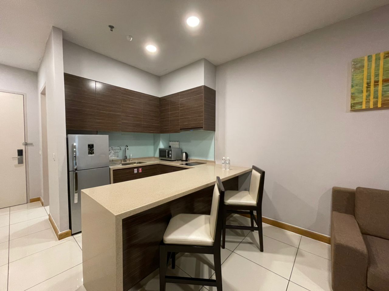 A compact kitchen with a central island, two chairs, a refrigerator, and a microwave.