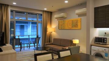 A hotel room with a sofa, a dining table, chairs, a TV, a washing machine, and an air conditioning unit.