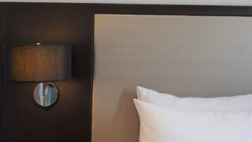 A hotel room with a bed, a wall-mounted lamp, and a painting above the bed.
