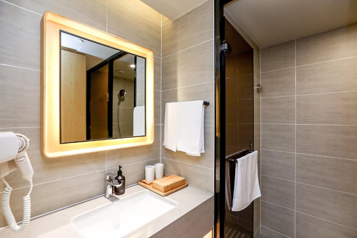 A modern bathroom with a large mirror, a sink, a hairdryer, and a shower area.
