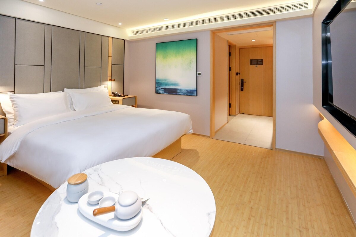 A modern hotel room with a large bed, a dining table with a white marble top, and a painting on the wall.