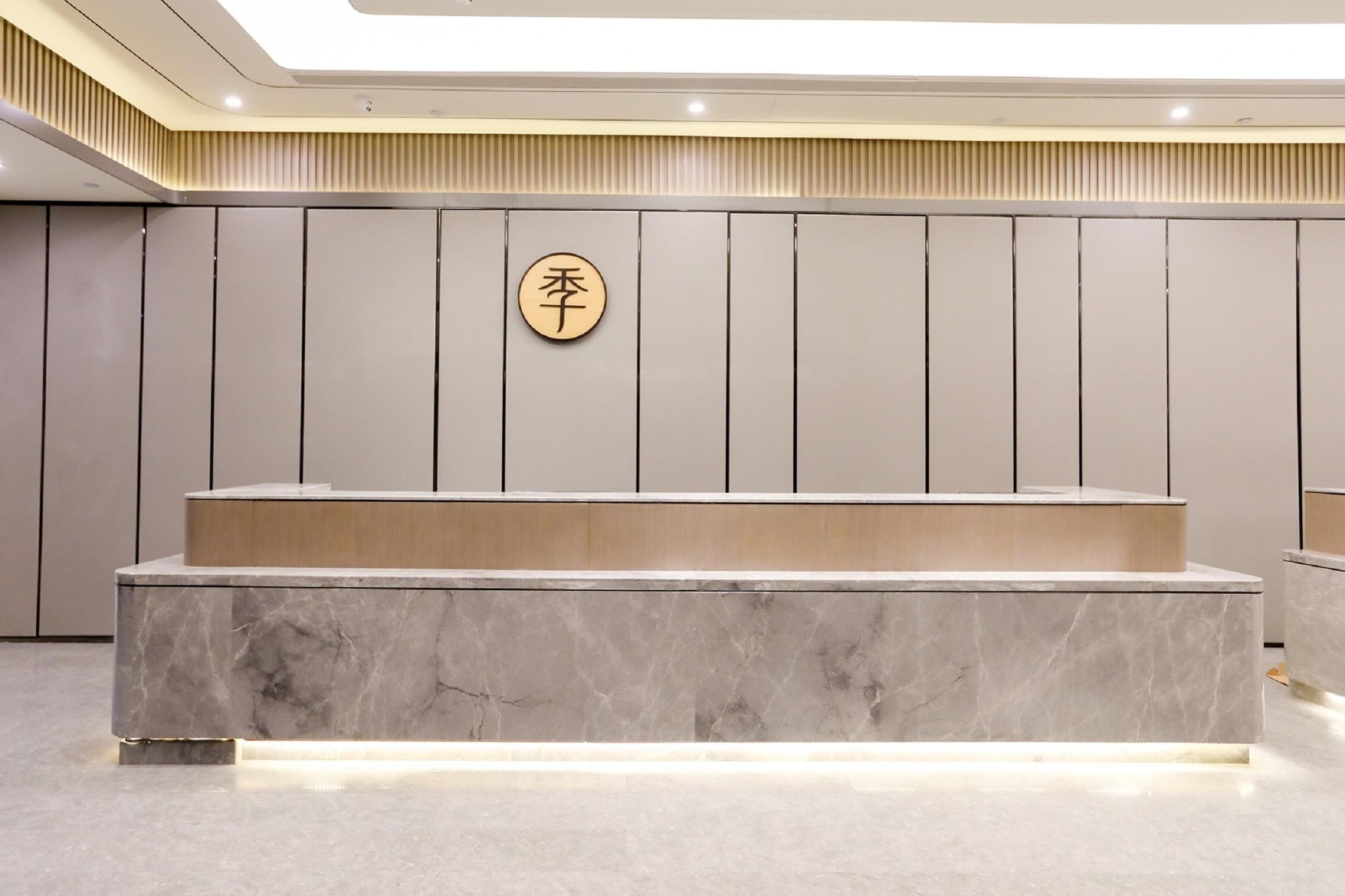 A reception desk with a marble top and a wooden counter, a wall-mounted sign with Chinese characters, and a ceiling with recessed lighting.