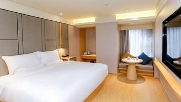 A modern hotel room with a large bed, a small table, a sofa, and a TV.