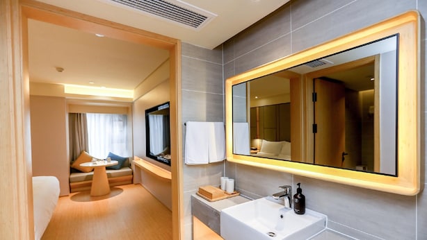 A modern hotel bathroom with a large mirror, a sink, and a seating area with a table and cushions. - Ji Hotel (Chongqing)
