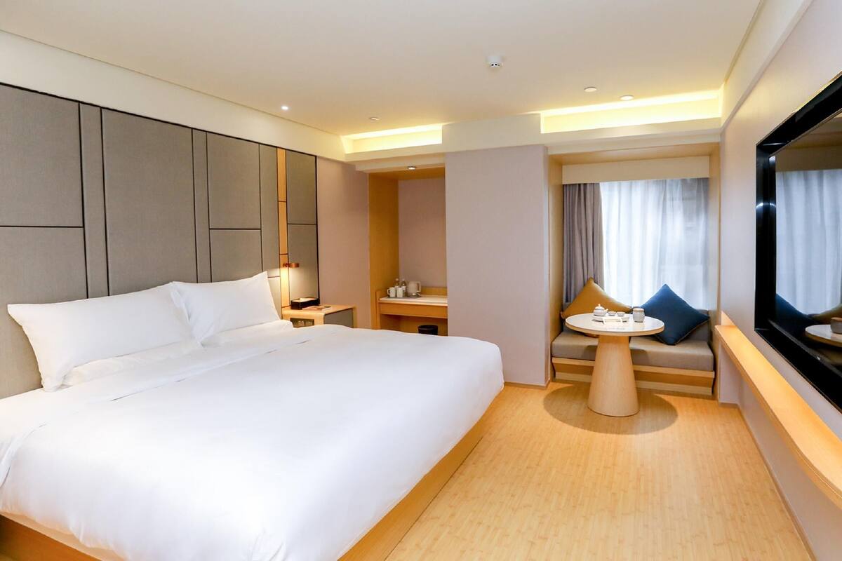 A modern hotel room with a large bed, a small table, a sofa, and a TV.