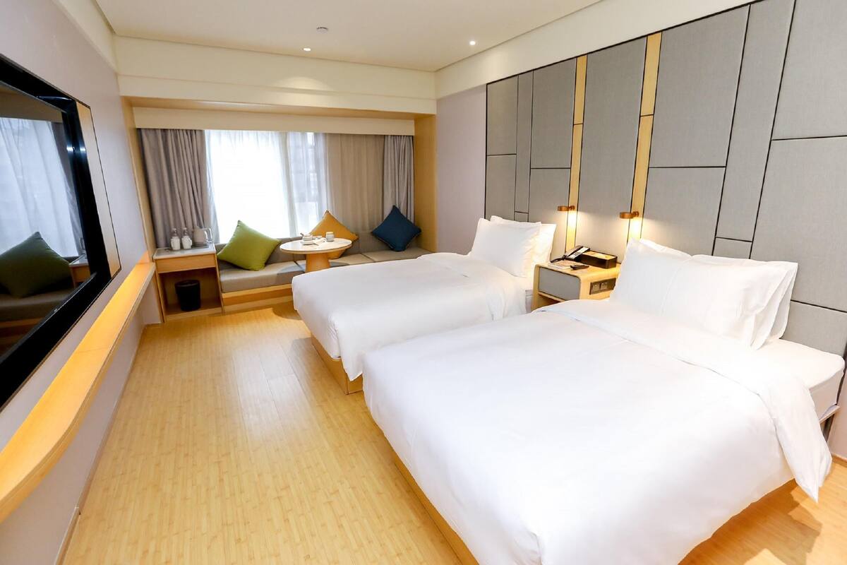 A hotel room with two beds, a TV, a small table with a chair, and a window with curtains.