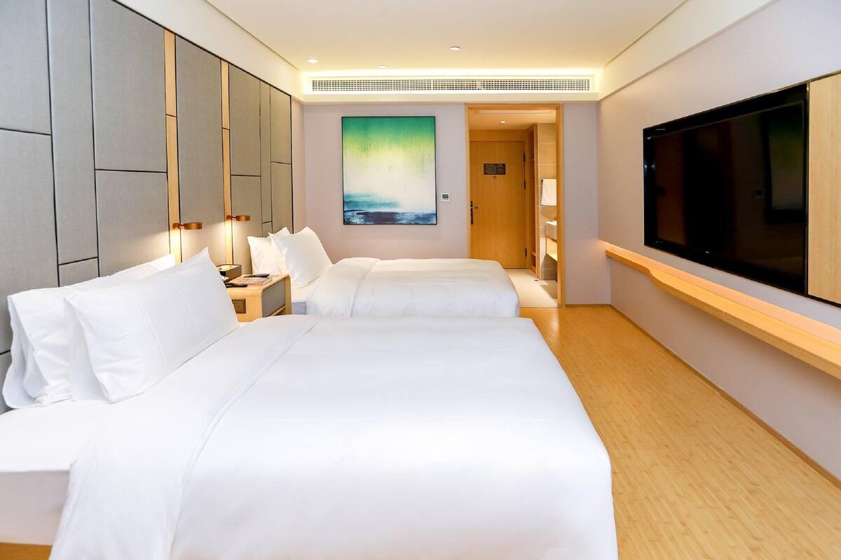 A hotel room with two beds, a large TV, and a painting on the wall.