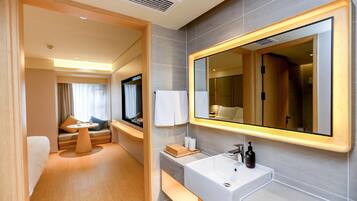 A modern hotel bathroom with a large mirror, a sink, and a seating area with a table and cushions.