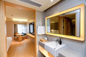A modern hotel bathroom with a large mirror, a sink, and a seating area with a table and cushions. - Ji Hotel (Chongqing)