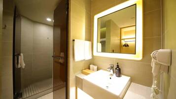 Un baño de hotel con cabina de ducha de vidrio, un lavamanos con espejo y un secador de pelo en la pared.