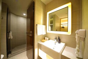 A hotel bathroom with a glass shower enclosure, a sink with a mirror, and a hairdryer on the wall. - Ji Hotel (Chongqing)
