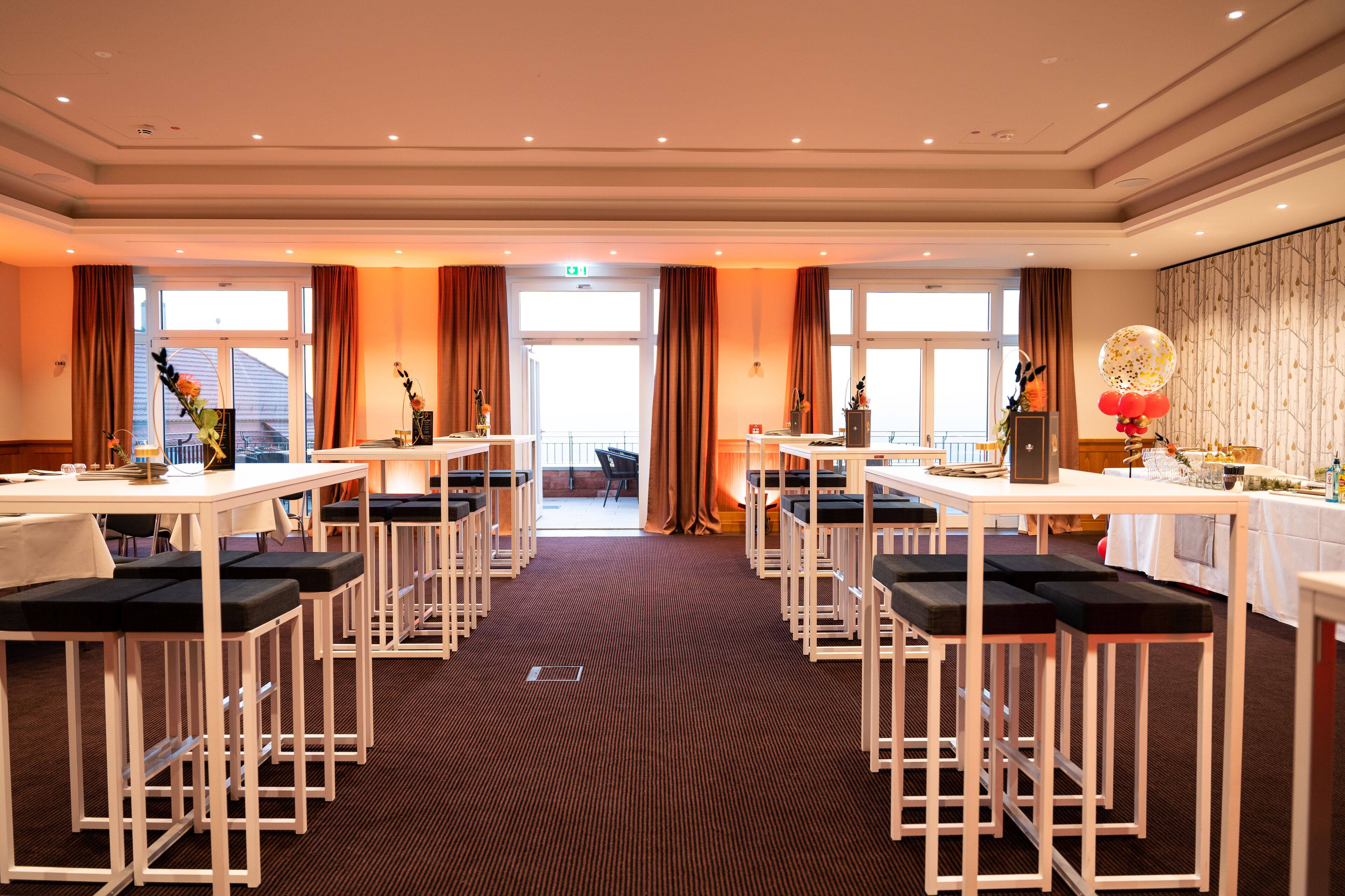 Un hall d’hôtel spacieux, doté de nombreux tabourets de bar, de tables et d’une grande fenêtre donnant sur l’extérieur.