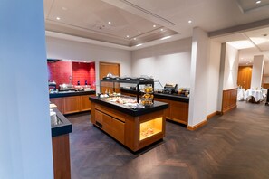 Una cocina moderna de hotel con un sistema tipo bufé, armarios de madera y una isla central con vitrina de vidrio.