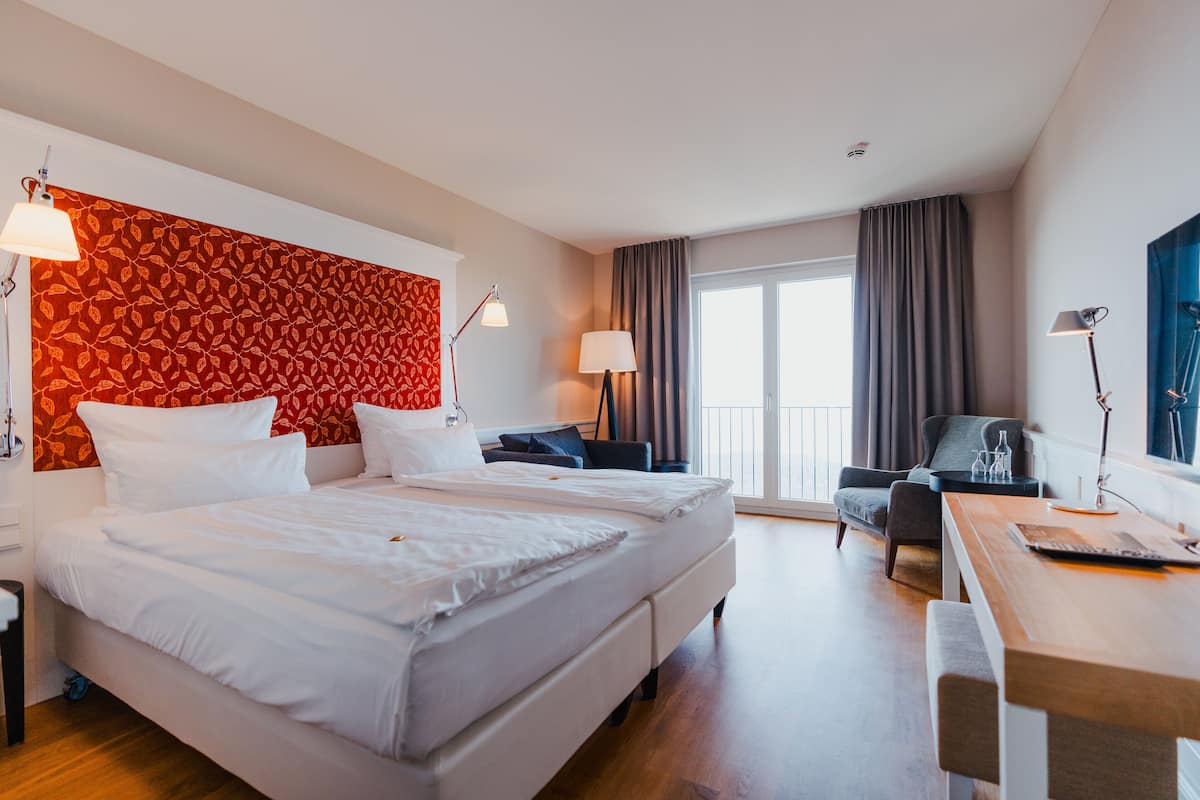A hotel room with a large bed, a desk, a chair, and a view of the outdoors.