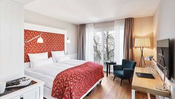 Habitación de hotel con cama, escritorio, silla, televisor y ventana con cortinas.