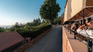 Una terrazza con posti a sedere all'aperto, un albero grande e vista sul mare.