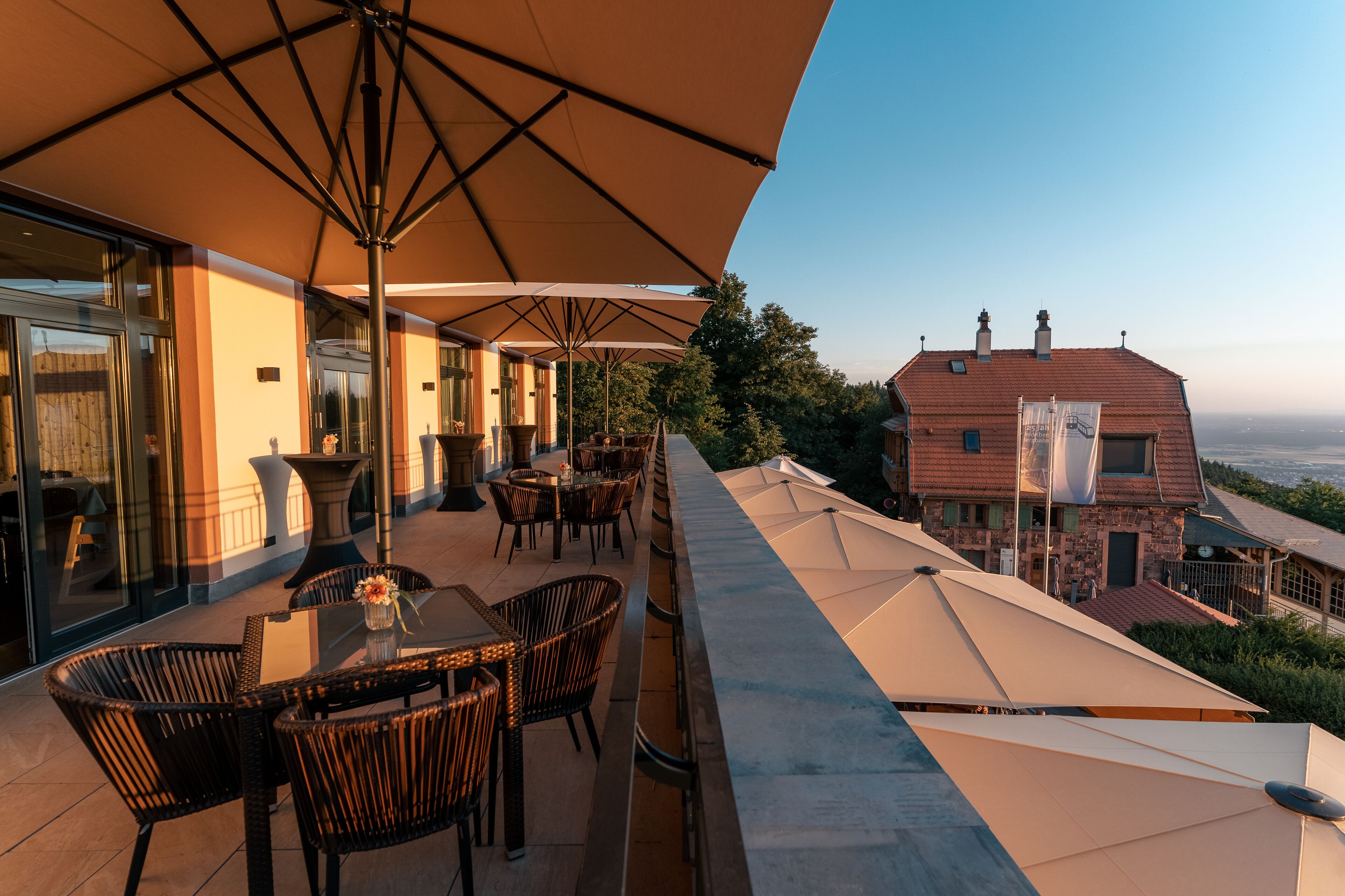 An outdoor terrace with tables and chairs under large umbrellas, overlooking a scenic view.