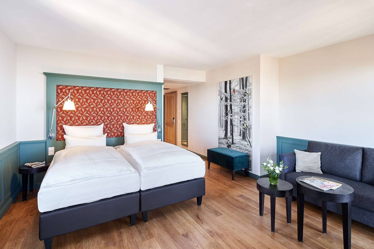 A hotel room with a double bed, two bedside tables, a sofa, and a large abstract painting.