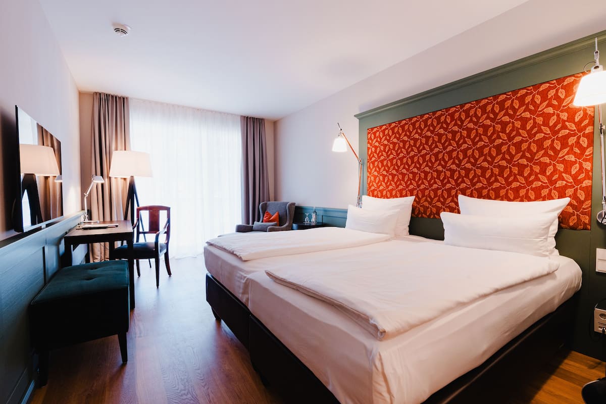 A hotel room with two beds, a desk, a chair, a lamp, and a window with curtains.