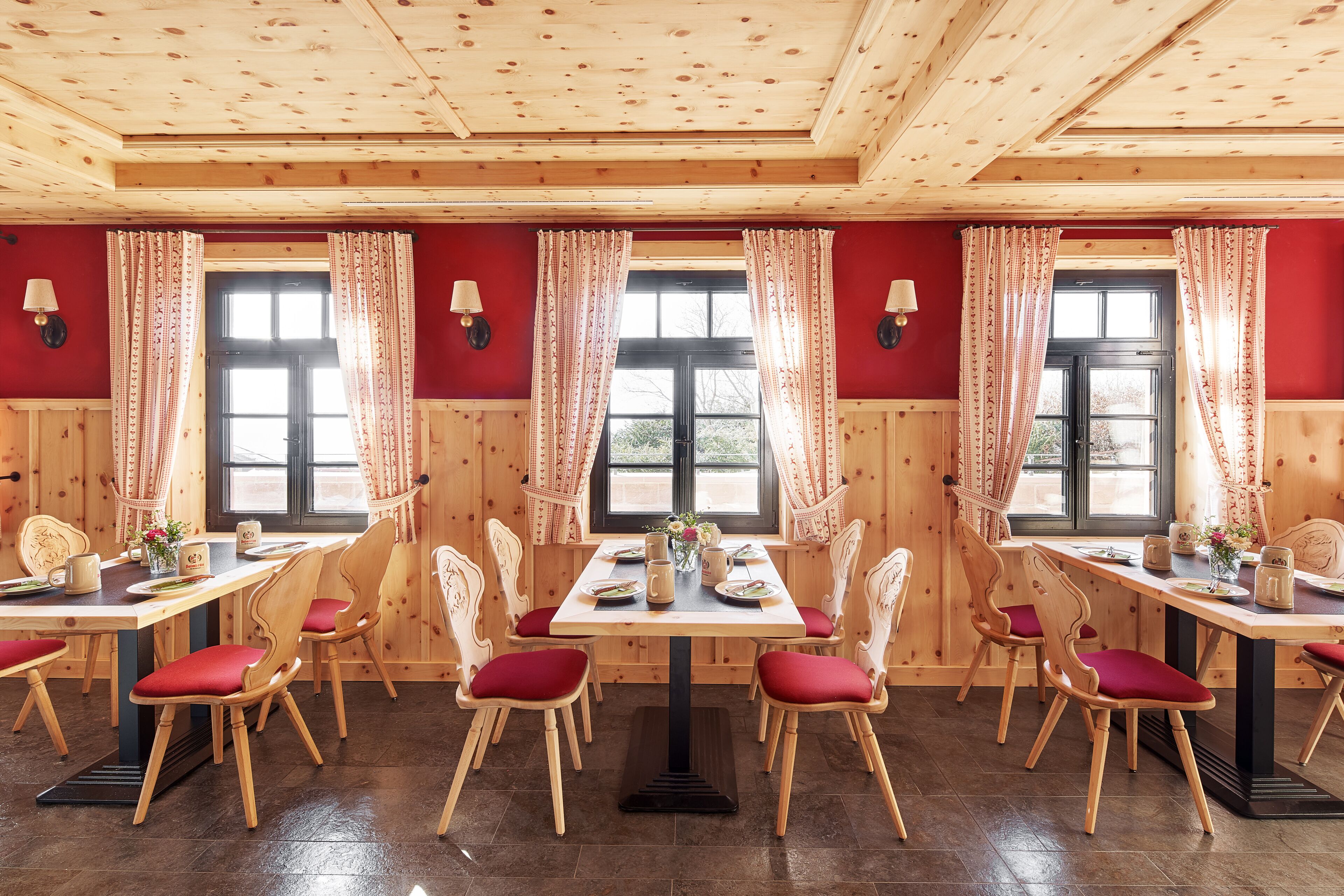 A dining area with wooden tables and chairs, red cushions, and a window with curtains.