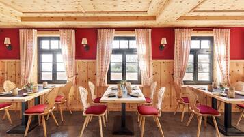 A dining area with wooden tables and chairs, red cushions, and a window with curtains.