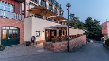 A hotel with outdoor seating, a brick facade, and a balcony with umbrellas.